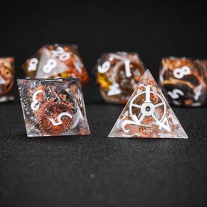 May include: A collection of polyhedral dice with a steampunk theme. The dice are clear with copper-colored gears and flakes inside. White numbers and symbols are visible on the dice. One die is a pyramid shape.