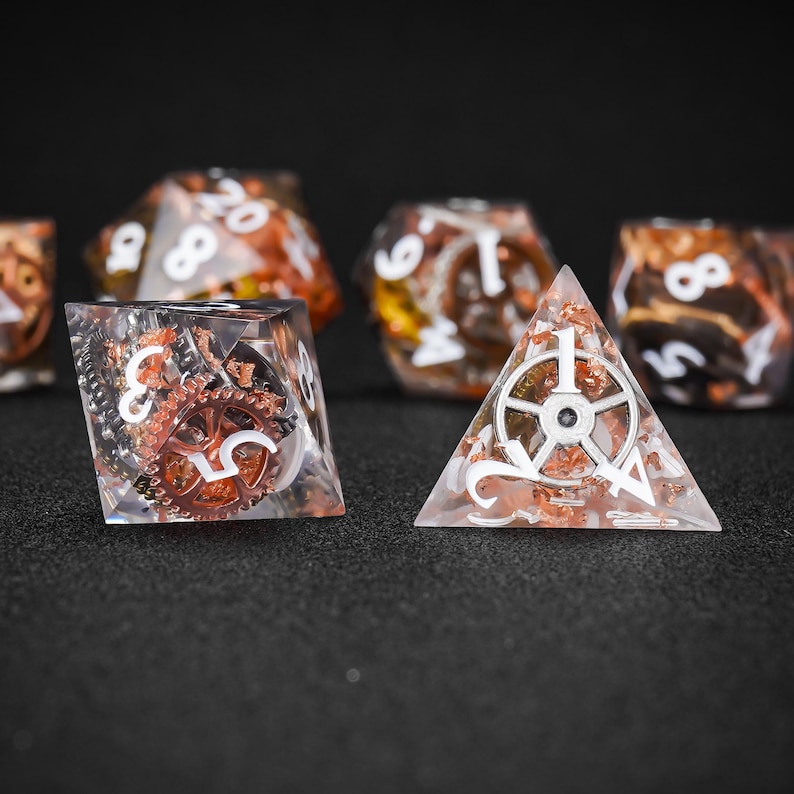 May include: A collection of polyhedral dice with a steampunk theme. The dice are clear with copper-colored gears and flakes inside. White numbers and symbols are visible on the dice. One die is a pyramid shape.