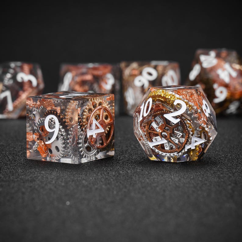 May include: Set of clear resin dice with embedded gears and metallic accents. The dice feature white numbers and a steampunk aesthetic. Includes a six-sided die and a multi-sided die.