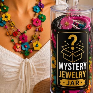 Può includere: Un barattolo cilindrico trasparente riempito con vari gioielli colorati, con un'etichetta nera che mostra un punto interrogativo, l'icona di una scatola aperta e il testo MYSTERY JEWELRY JAR. Accanto, una collana a più fili con fiori in legno.