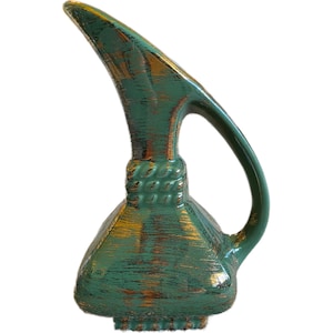 May include: A teal-colored ceramic pitcher with a long, curved spout and a handle. The pitcher has a textured surface with gold accents, and a decorative rope-like detail around the neck. The base is a squared shape.
