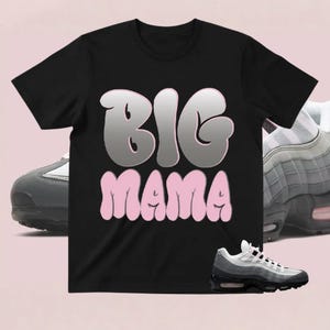 May include: Black t-shirt with the words "BIG MAMA" in a bubble font. The word "BIG" is in a silver color with a pink outline, and the word "MAMA" is in pink. Sneakers are in the background.