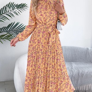 Puede incluir: Vestido amarillo de manga larga con estampado floral en rosa y morado. El vestido presenta una falda plisada, una cintura anudada y un cuello alto. El vestido es de largo midi.