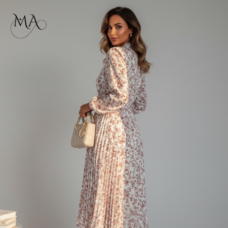 Puede incluir: Vestido largo con estampado floral, falda plisada y mangas largas. El vestido presenta un cuello alto y una mezcla de patrones blancos y florales. Se sostiene en la mano un peque&ntilde;o bolso de mano color crema con detalles dorados.