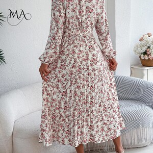 Puede incluir: Vestido largo de manga larga, plisado, con estampado floral rosa sobre fondo marfil. El vestido presenta un cuello alto, cintura entallada y falda fluida. Adecuado para diversas ocasiones.