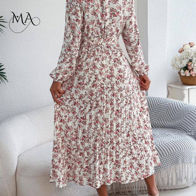 Puede incluir: Vestido largo de manga larga, plisado, con estampado floral rosa sobre fondo marfil. El vestido presenta un cuello alto, cintura entallada y falda fluida. Adecuado para diversas ocasiones.