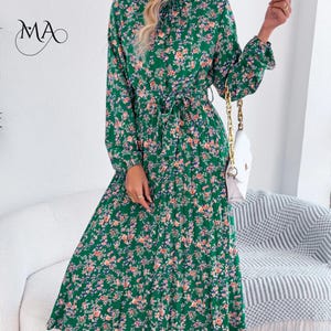 Puede incluir: Un vestido largo verde con estampado floral, cuello alto y cintur&oacute;n anudado a la cintura. El vestido presenta un patr&oacute;n de peque&ntilde;as flores rosas y naranjas con hojas azules. Tambi&eacute;n se ve un bolso blanco con una cadena dorada.