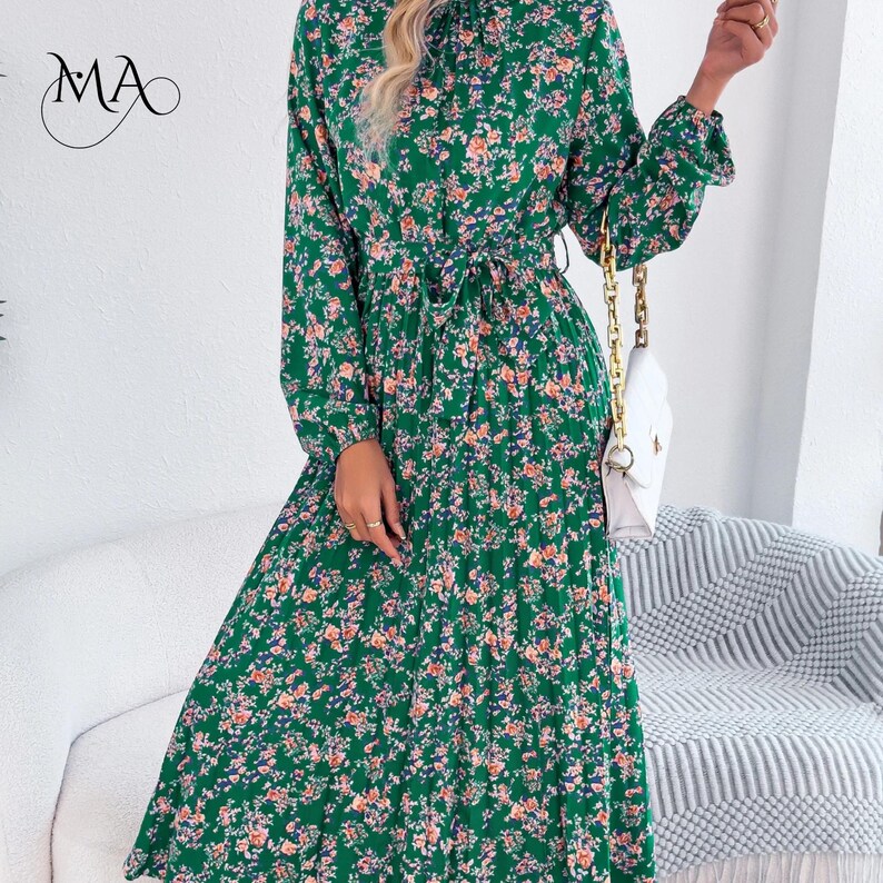 Puede incluir: Un vestido largo verde con estampado floral, cuello alto y cintur&oacute;n anudado a la cintura. El vestido presenta un patr&oacute;n de peque&ntilde;as flores rosas y naranjas con hojas azules. Tambi&eacute;n se ve un bolso blanco con una cadena dorada.