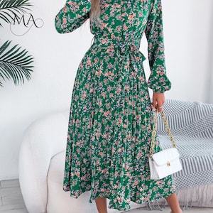 Puede incluir: Vestido midi verde con estampado floral, mangas largas y falda plisada. El vestido tiene una cintura anudada y un cuello alto. Se complementa con un bolso blanco acolchado con cadena dorada. El vestido mide aproximadamente 110 cm de largo.