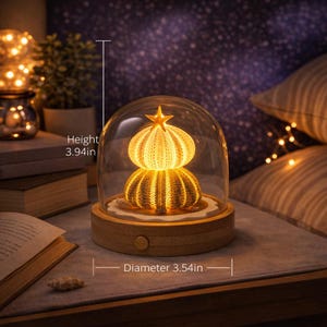 Puede incluir: Luz de noche decorativa con dos estructuras iluminadas en forma de erizo de mar bajo una cúpula de cristal. La base de madera tiene 9 cm de diámetro y 10 cm de altura. Una estrella adorna el erizo superior.