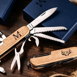 May include: A multi-tool knife with a wooden handle, featuring various blades and tools like a saw and scissors. The knife is engraved with the initials "M IV". A smaller knife with "CH" and a deer antler design is also visible.