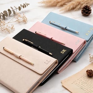 May include: Four rectangular notebooks in beige, black, pink, and light blue, each featuring a matching pen held in a loop on the front cover. Each notebook is personalised with gold or silver embossed initials on the bottom right corner.