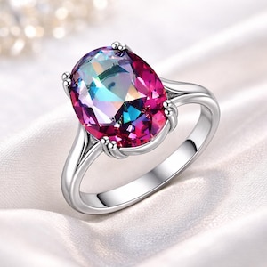 Peut inclure: Une bague en argent ornée d'une grosse pierre ovale aux couleurs vives : rose, violet, bleu et vert. L'anneau en argent poli soutient la pierre, maintenue par quatre griffes. Un bijou saisissant.