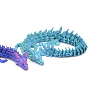 Könnte beinhalten: Drei bewegliche Drachenfiguren in Blau- und Lilatönen werden vor einem weißen Hintergrund gezeigt. Die Drachen haben eine stachelige, kristalline Textur, wobei der größte eingerollt ist. Die Farbverläufe verleihen dem detaillierten Design Tiefe.