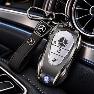 Pode incluir: Uma capa metálica cinza-escura para chave de carro Mercedes-Benz com um painel central texturizado em prata e branco com três botões. Inclui uma alça de couro preta com o logótipo da Mercedes em prata e um mosquetão de metal escuro.
