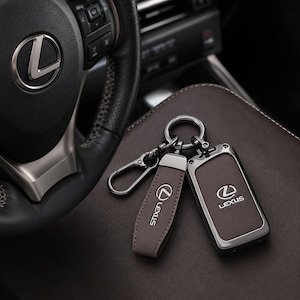 Peut inclure: Un étui de clé de voiture Lexus en cuir marron foncé et une lanière de porte-clés en cuir assortie avec un anneau et un fermoir en métal gris bronze. Les deux articles présentent le logo Lexus et le mot Lexus gravés en argent.