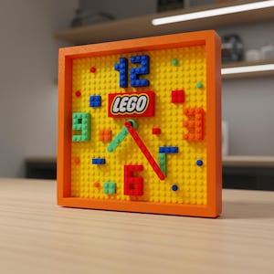 Könnte beinhalten: Eine quadratische Uhr mit orangefarbenem Rahmen und einem gelben Zifferblatt aus Lego-Steinen. Die Uhr hat blaue Zahlen, rote und grüne Zeiger und ein rotes Lego-Logo. Die Zahlen 12 und 6 sind sichtbar.