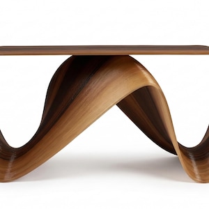 Peut inclure: Une table basse moderne et sculpturale avec un design unique et fluide. La table est faite de bois stratifié, avec un dessus brun foncé et une base incurvée plus claire. Dimensions: environ 122 cm de long et 41 cm de haut.