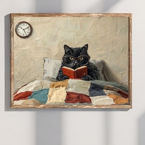 以下が含まれることがあります： メガネをかけた黒猫がベッドで赤い本を読んでいる額入りの絵。猫はカラフルなパッチワークのキルトの下にいます。ベッドの上には時計が壁に取り付けられています。