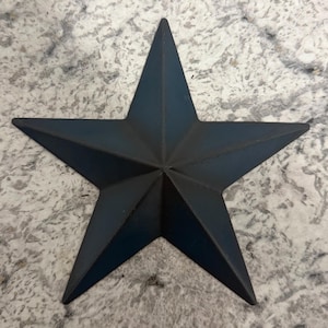 May include: A five-pointed star ornament with a matte dark blue finish. The star features a dimensional, raised center point that radiates outward to each of the five sharp tips, creating a geometric, multi-faceted surface appearance.