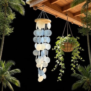 May include: A hanging wind chime featuring multiple circular, translucent, light blue and white shell-like discs suspended from a round wooden top piece by thin strings, creating a cascading, layered vertical arrangement of decorative elements.