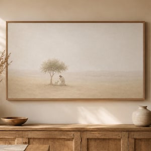 Könnte beinhalten: Ein rechteckiger Kunstdruck in einem hellen Holzrahmen mit einer Landschaftsmalerei in gedämpften Beigetönen. Die Szene zeigt einen einzelnen Baum auf einem weiten, dunstigen Feld mit einer knienden Figur neben einem kleinen Tier.