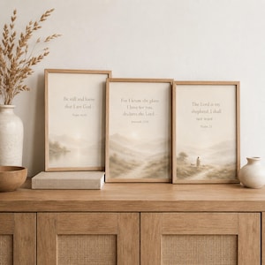 May include: Three rectangular framed wall art prints featuring beige landscape illustrations and religious text. The prints display the verses Be still and know that I am God, For I know the plans I have for you, and The Lord is my shepherd.