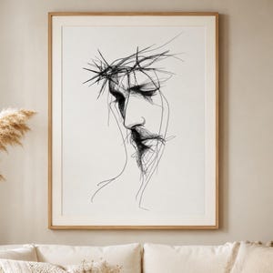 Könnte beinhalten: Ein gerahmter Schwarz-Weiß-Kunstdruck. Das Kunstwerk zeigt ein Seitenprofil einer Person mit einer Dornenkrone. Der Zeichenstil ist minimalistisch, mit Fokus auf Gesicht und Hals. Der Rahmen hat eine hellbraune Farbe.