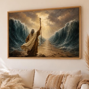 Può includere: Una stampa artistica incorniciata raffigurante una figura con una tunica beige fluida, in piedi su un sentiero sabbioso tra due imponenti onde oceaniche blu scuro, che tiene un alto bastone di legno verso una luce dorata nel cielo nuvoloso.