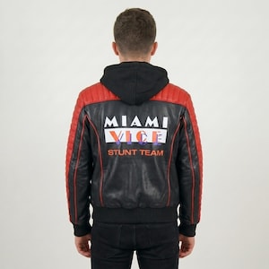 Peut inclure: Une veste en cuir noire et rouge avec une capuche noire et des panneaux d'épaules côtelés. Le dos présente le texte blanc MIAMI VICE avec le mot VICE en orange et violet, suivi du texte orange STUNT TEAM sur le panneau arrière inférieur.