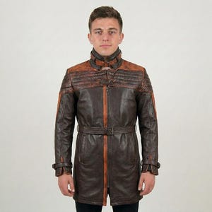May include: A long, dark brown leather jacket featuring a high collar with a buckle strap, quilted shoulder panels in a distressed rust-brown tone, a central zipper closure with a rust-colored trim, and a matching leather belt at the waist.