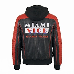 May include: A black leather jacket with a black hood, featuring red quilted panels on the sleeves and back. The back displays the white text MIAMI VICE with the word VICE in red and blue, followed by the orange text STUNT TEAM. It has a ribbed hem.