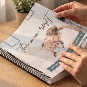 May include: A spiral-bound journal titled "the mom reset" with a photograph of a mother and child. The journal is open, revealing the image and text. The cover features a soft, neutral color palette.