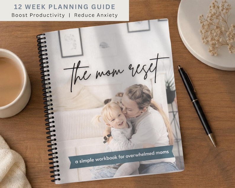 May include: A spiral-bound planner titled "The Mom Reset" with the text "12 Week Planning Guide" and "Boost Productivity | Reduce Anxiety." The cover features a photo of a mother and child. A pen and a cup of coffee are on a wooden surface.