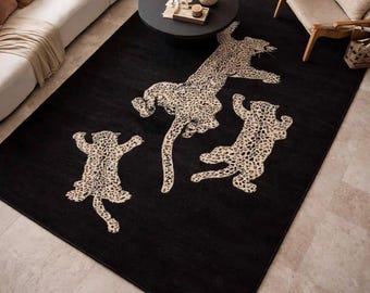 May include: A large rectangular area rug featuring a solid black background with three cream and brown leopard-patterned big cats depicted in a playful, leaping motion. The rug is positioned on a light-colored tile floor in a living room.