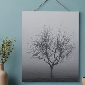 Könnte beinhalten: Schwarz-Weiß-Leinwanddruck eines kahlen Baumes in einer nebligen Landschaft. Der Baum ist im Zentrum, mit einer detaillierten Silhouette vor einem gedämpften Hintergrund. Der Druck wird an einer Schnur aufgehängt.