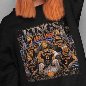 May include: Black sweatshirt featuring a graphic of basketball players with the text "KINGS OF NEW YORK." The design includes the numbers 8, 11, 25, 32, and 3. The sweatshirt has a crew neck and long sleeves.