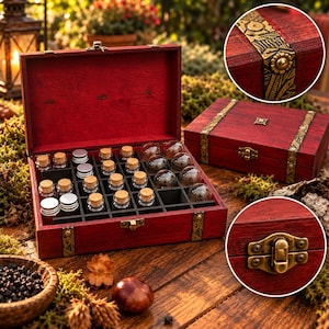 May include: A rectangular red wooden storage box with a hinged lid, featuring brass-colored metal latches and decorative embossed bands. The interior contains a grid of compartments holding small glass vials with cork stoppers and round glass spheres.
