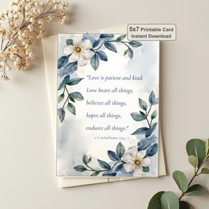 Puede incluir: Una tarjeta imprimible de 5x7 pulgadas con un borde floral de acuarela con flores blancas y hojas azul grisáceo. El texto dice: Love is patient and kind. Love bears all things, believes all things, hopes all things, endures all things. 1 Corinthians 13:4-7.