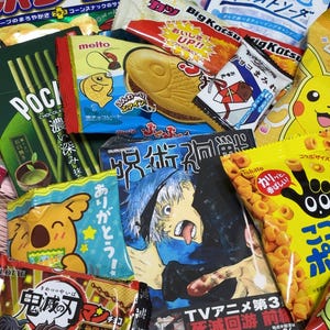 Peut inclure: Un assortiment d'en-cas japonais, comprenant des Pocky, des gâteaux en forme de poisson et des chips. Les emballages sont colorés avec des personnages de dessins animés et du texte japonais. Les snacks sont de formes et de tailles variées.
