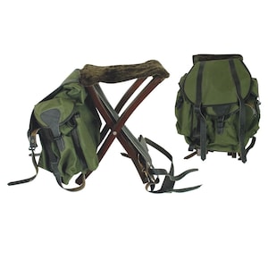 May include: Two green canvas backpacks with black leather straps and buckles. One backpack is attached to a folding wooden stool with a brown, textured seat. The other backpack is separate.