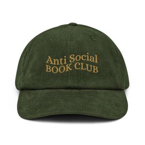 May include: A green corduroy baseball cap with the embroidered text "Anti Social BOOK CLUB" in a gold color. The cap has a curved brim and a structured crown.