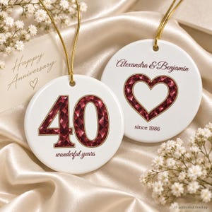 Puede incluir: Dos adornos redondos de cerámica blanca con cordones dorados. Uno muestra el número 40 en un patrón de gemas facetadas de color rojo oscuro con el texto wonderful years. El otro presenta un corazón con el mismo patrón y Alexandra & Benjamin since 1986.