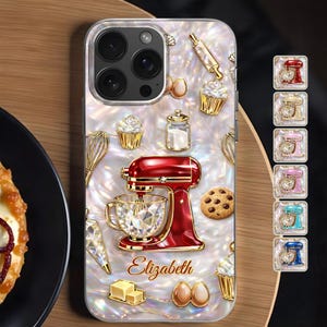 May include: A clear phone case featuring a red stand mixer, cupcakes, and baking tools. The case has a pearlescent background with gold accents. The name "Elizabeth" is written in gold script. Additional color options are displayed on the right.