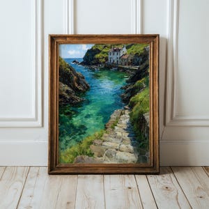 May include: A framed oil painting depicting a coastal scene with stone steps leading down to a turquoise inlet. The landscape features rugged cliffs, green vegetation, and white buildings nestled along the water's edge under a bright blue sky.