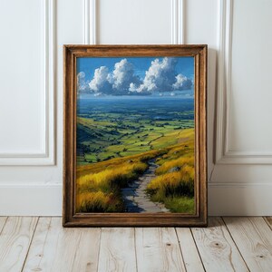 May include: A framed landscape painting depicting a stone path winding through golden grassy hills that lead to a vast green valley under a bright blue sky with large white clouds. The artwork is enclosed in a dark brown wooden frame.