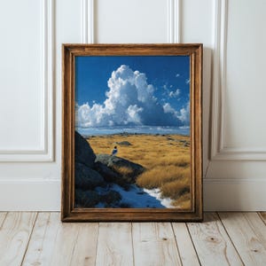 May include: A framed landscape print featuring a small bird perched on a large gray rock in a field of golden grass. The scene includes a patch of white snow in the foreground, dark rocky outcrops, and a bright blue sky with large white clouds.