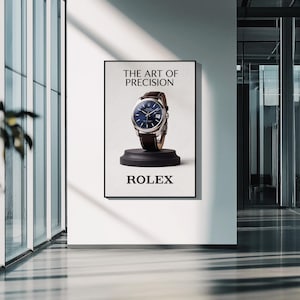 May include: A framed advertisement for a Rolex watch. The image features a wristwatch with a blue face and brown leather strap, displayed on a black pedestal. The text at the top reads "THE ART OF PRECISION" and the brand name "ROLEX" is at the bottom.