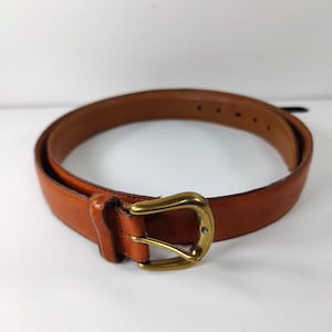 May include: A brown leather belt with a brass buckle. The belt is a medium brown color and has a classic design. The buckle is a gold color and has a rectangular shape.