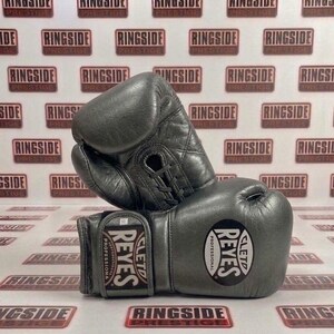 May include: A pair of gray leather boxing gloves, featuring the "REYES" logo and the words "PROFESSIONAL" and "CLETO". The gloves are laced up and appear to be new. The background has a repeating pattern of the word "RINGSIDE".